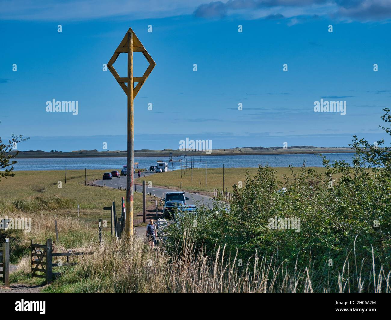 The marker at the causeway to Holy Island (Lindisfarne) in Northumberland, England, UK. Cars crossing the causeway are pictured in the distance. Stock Photo