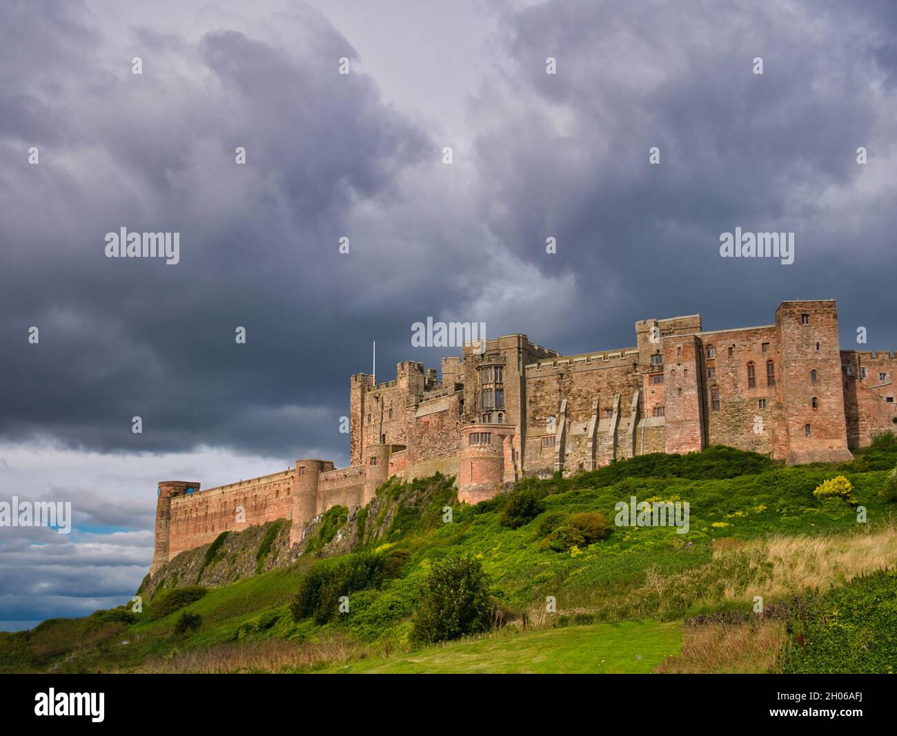 With sun shining through threatening clouds, the fortress-like south western face of the Grade 1 listed building, Bamburgh Castle in Northumberland,UK Stock Photo
