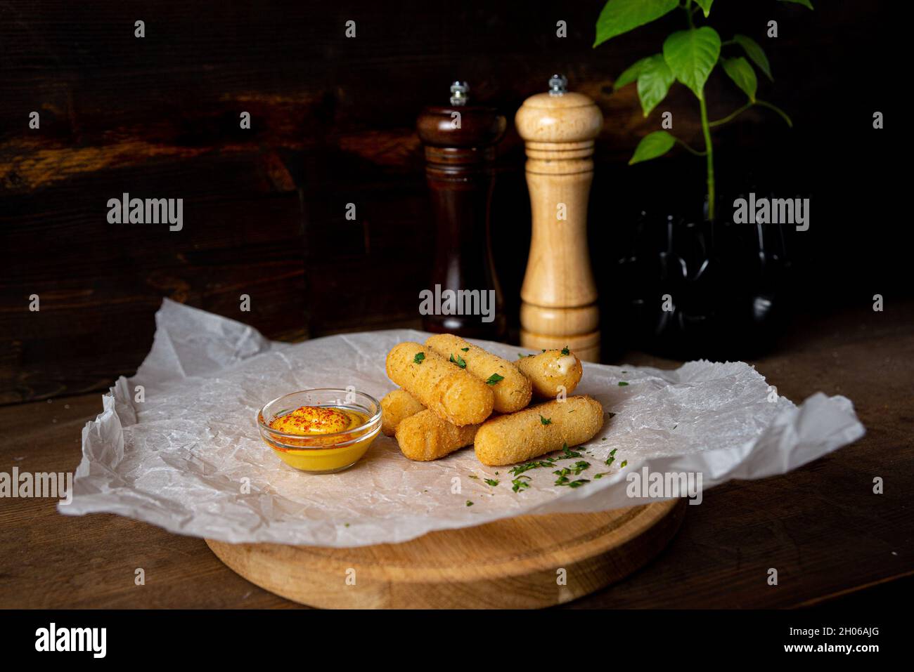 A portion of cheese sticks, served on a wooden board with mustard. Bar deep fried food. Shot in the interior of a bar against a dark wooden background Stock Photo