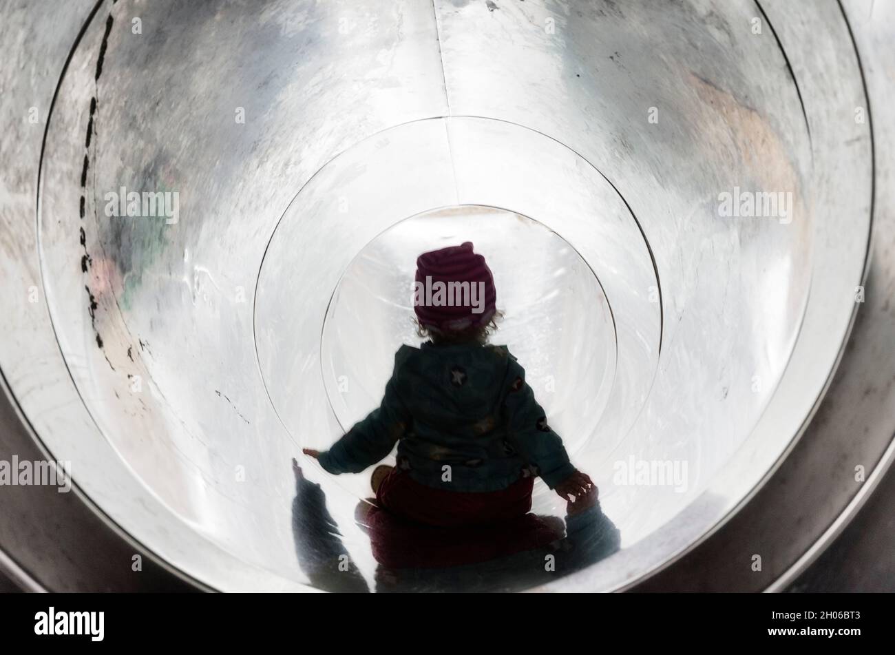Small girl in a metal slide.A little afraid Stock Photo