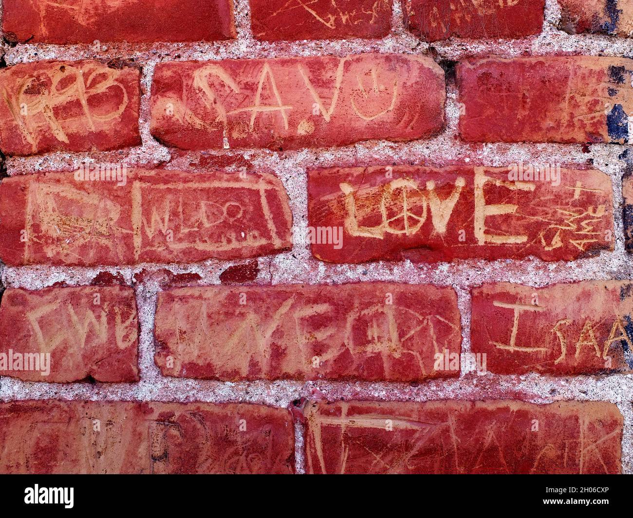 Detail of Old Red Brick Wall with Words Names and Love Scratched or Carved In Stock Photo