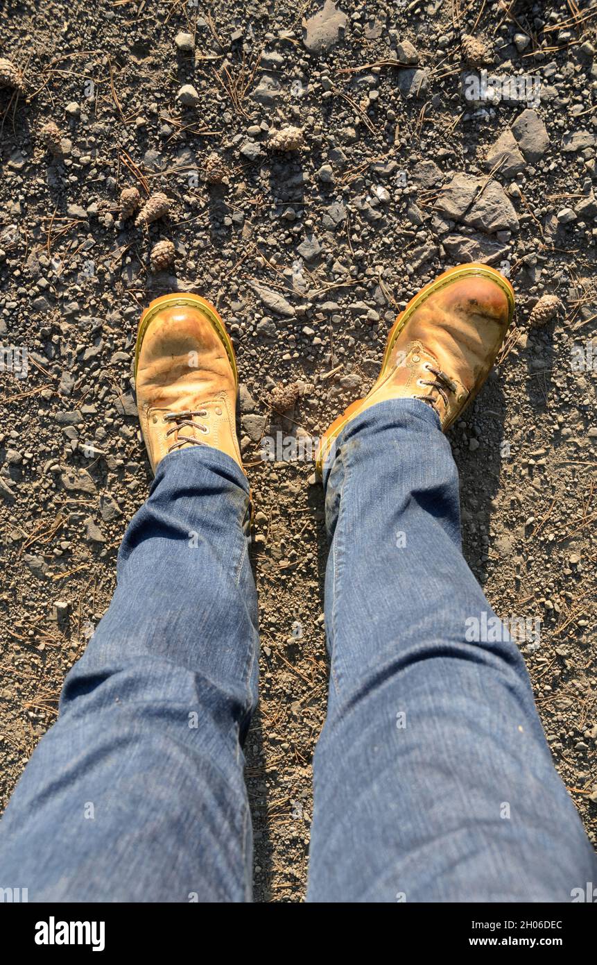 Looking down on a pair of jeans and yellow heavy duty boots on a gravel  road Stock Photo - Alamy