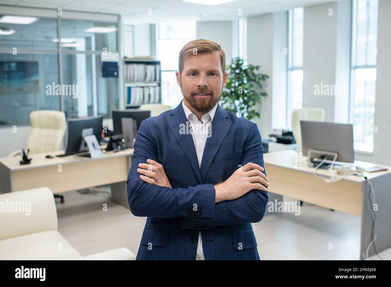 Happy young businessman with his arms crossed on chest standing against ...