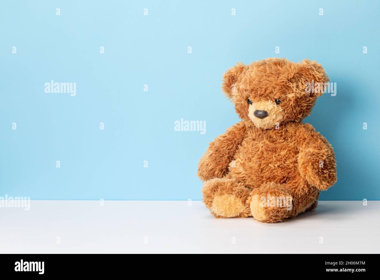 Teddy bear sits on a white table and blue background. Template Copy space for text. Stock Photo