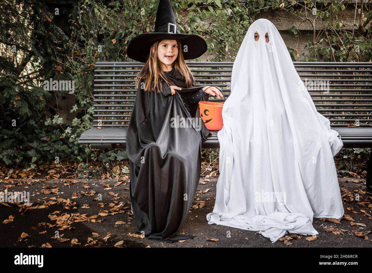 Young boy dressed in a bed sheet to be a ghost, and a young girl in witch costume holding a pumpkin pail for halloween. Stock Photo