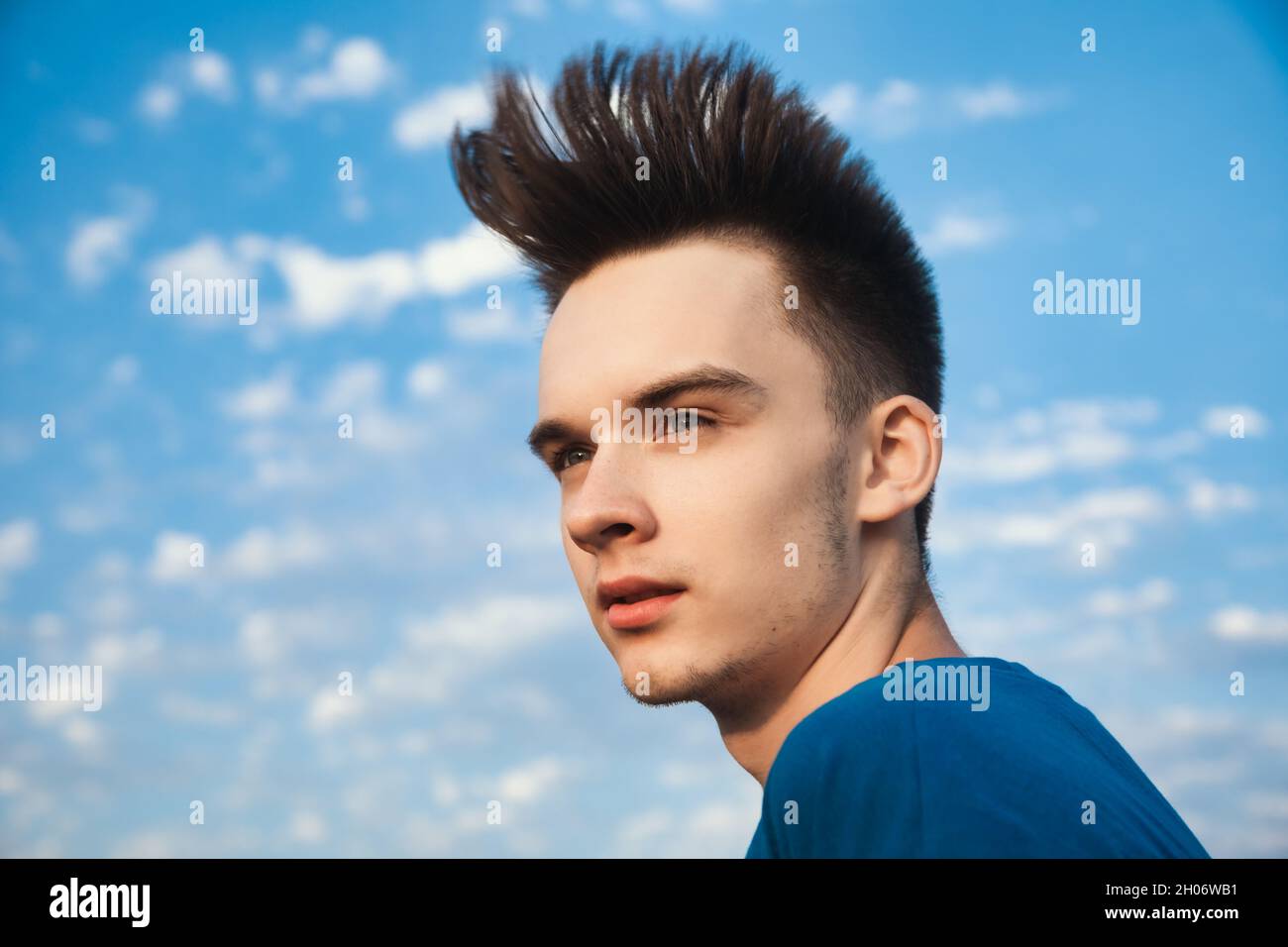 Outdoor portrait of teenager boy looking away with hair blowing in the wind against evening sky Stock Photo