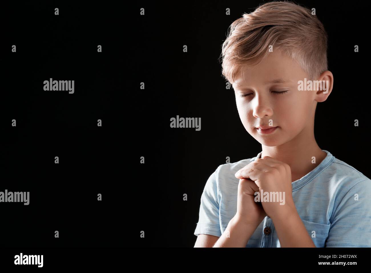 Little boy with hands clasped together for prayer on black background ...