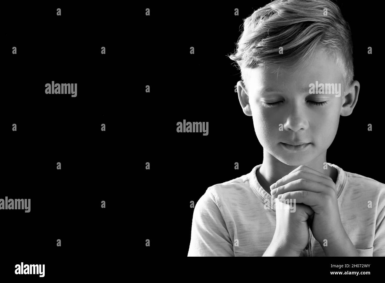 Little boy with hands clasped together for prayer on dark background ...