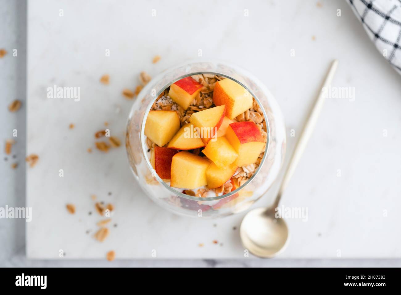Yogurt with granola and peach in jar on marble background, top view. Healthy dessert Stock Photo