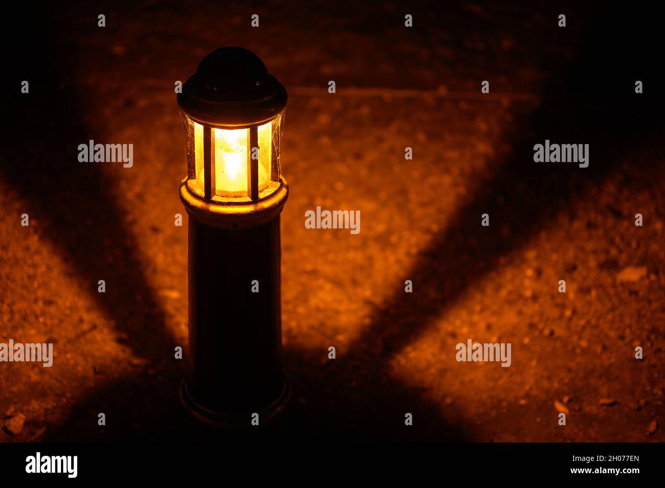 Lamp or light at night in a park with shadows in a circular pattern. The light illuminates a stony pathway. Off-center view of lamp with spider web. Stock Photo