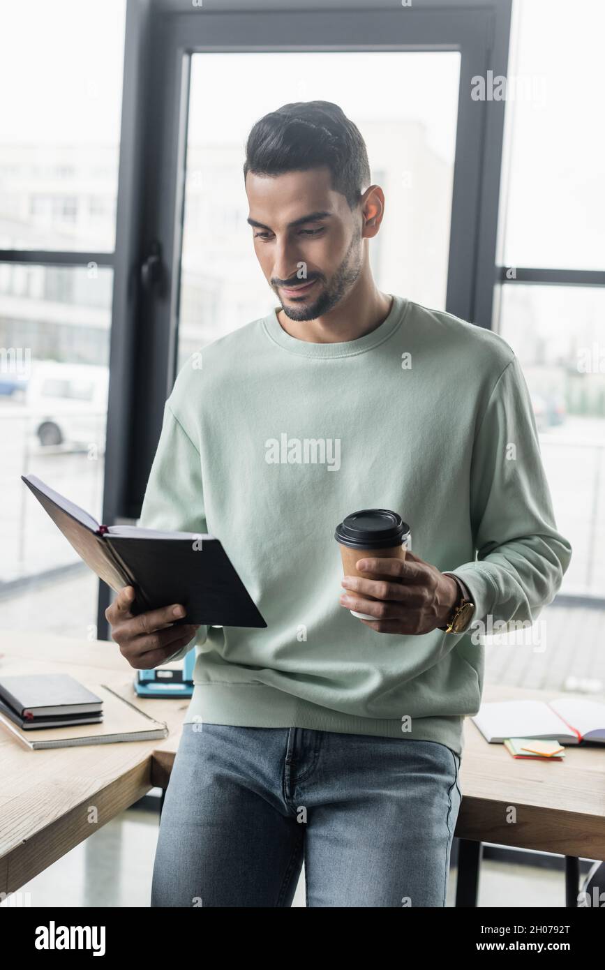 Young arabian businessman in casual clothes holding paper cup and notebook in office Stock Photo