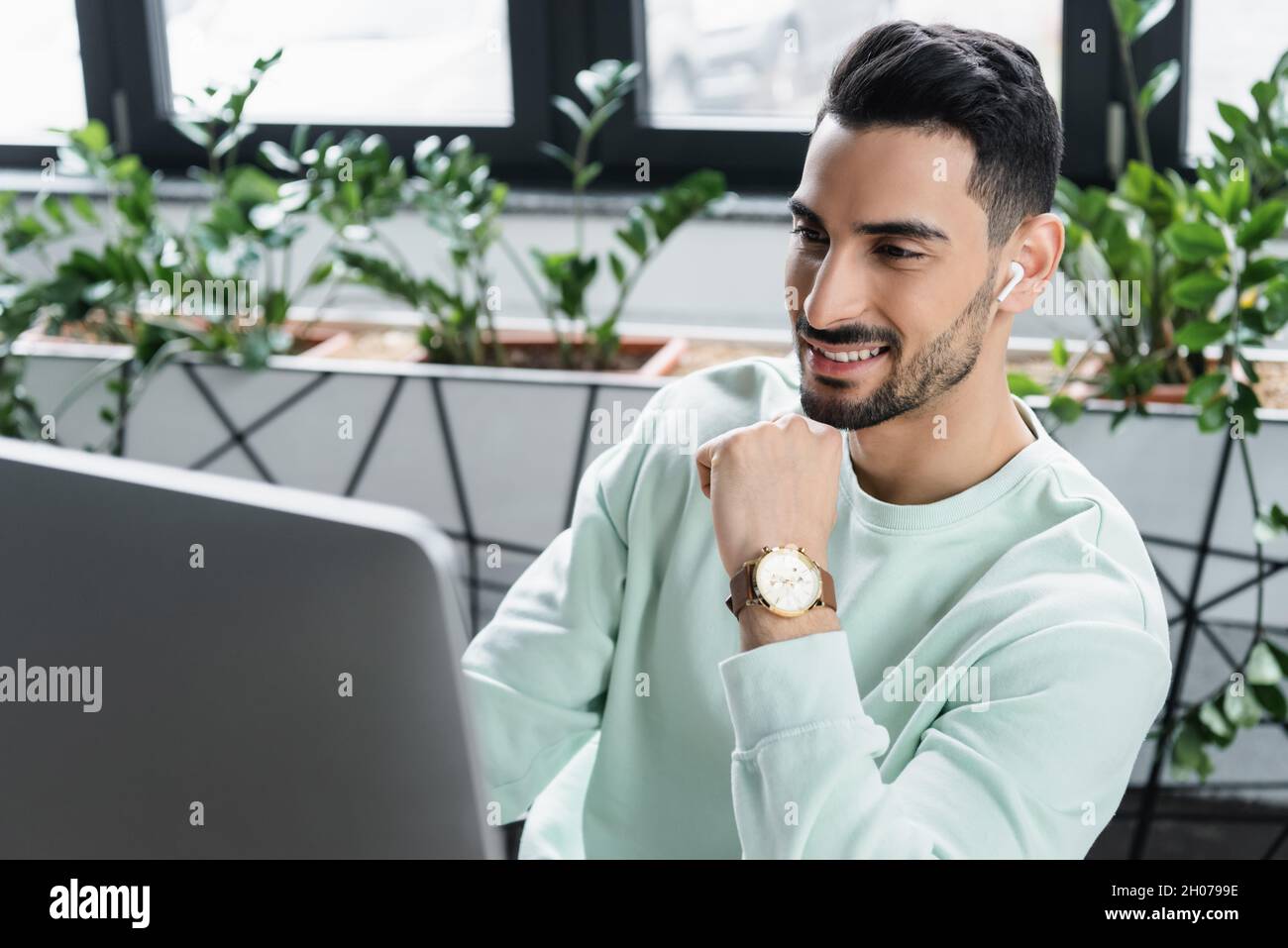 Positive arabian businessman in wireless earphone using blurred computer Stock Photo