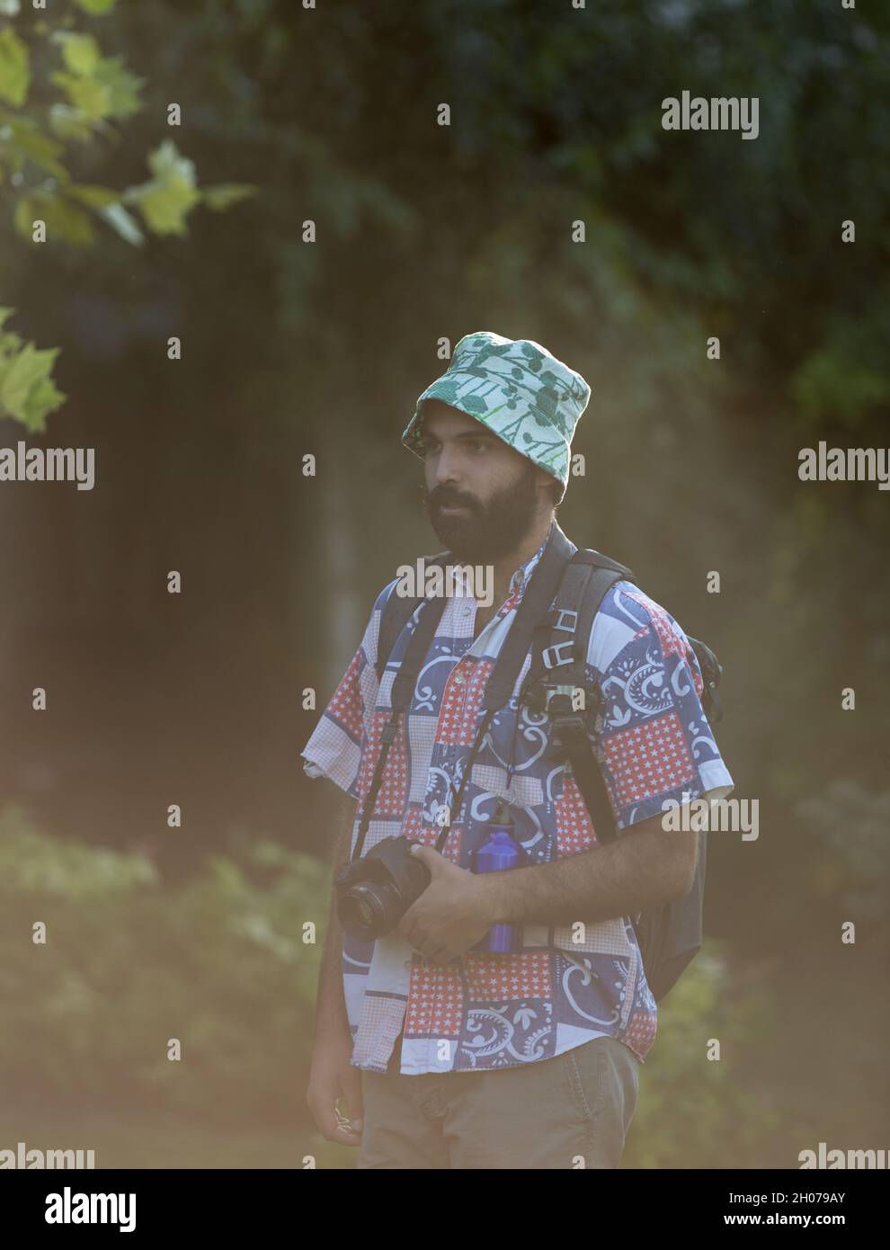Young man with backpack walking in forest and holding camera Stock Photo