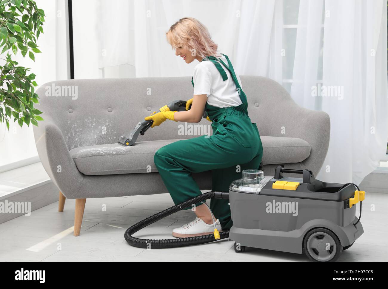 Female janitor removing dirt from sofa with upholstery cleaner in room Stock Photo Alamy