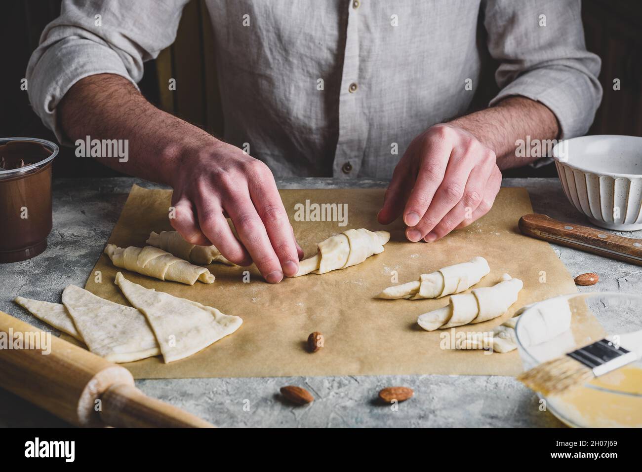 Homemade croissant preparing. Baker rolls the puff pastry stuffed with chopped almonds and hazelnut spread Stock Photo