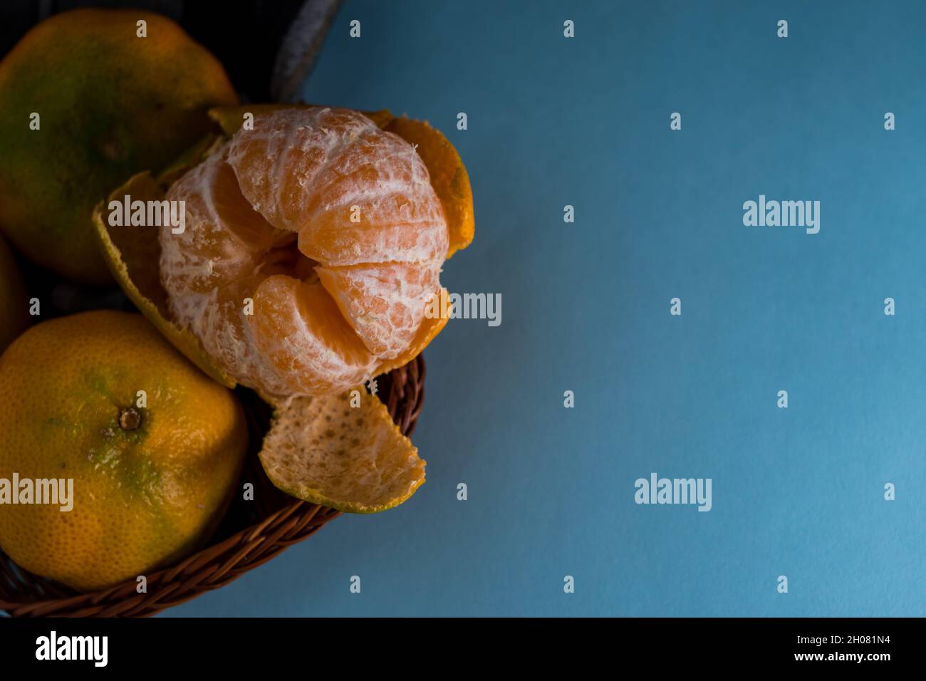 Some fresh tangerines in a basket on a blue surface with copy space Stock Photo