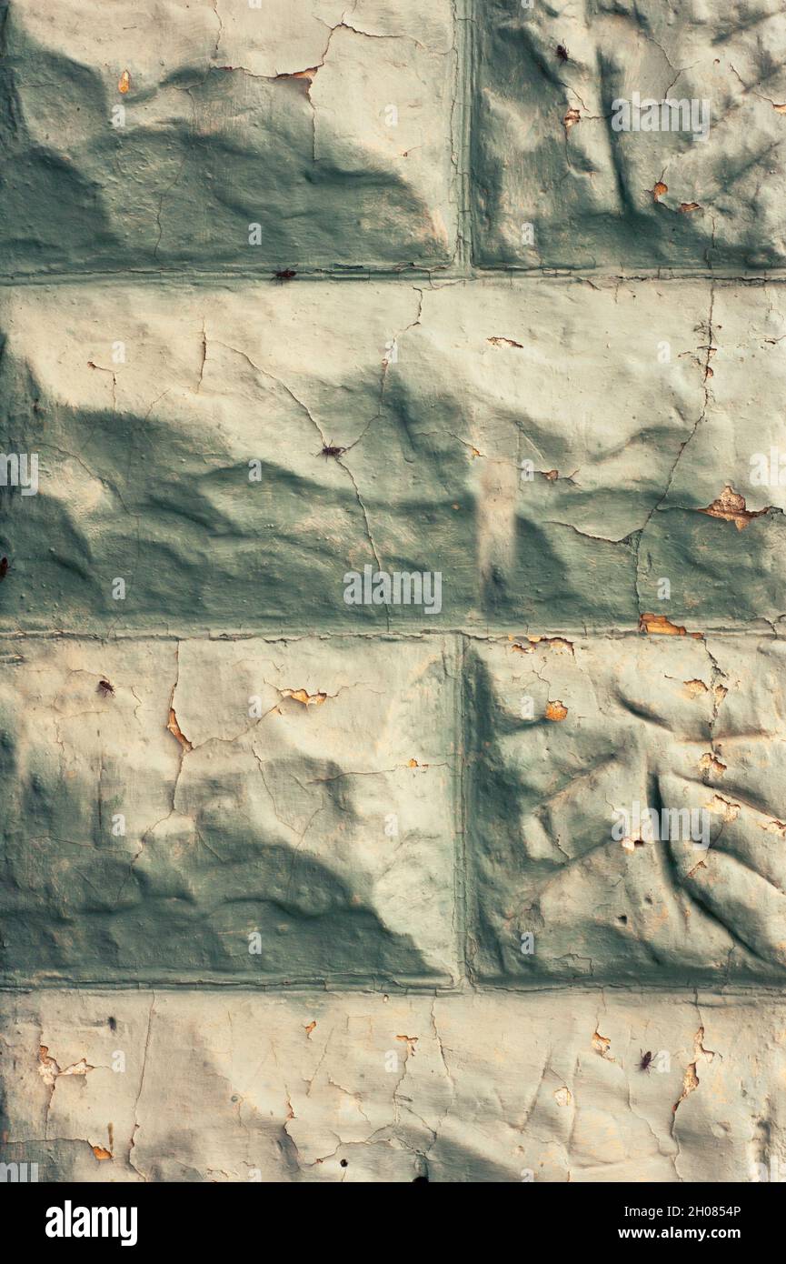 Old wall of gray cement blocks as seen in a closeup showing cracks, beetles, peeling paint, and protrusions with lots of dimensional texture. Stock Photo