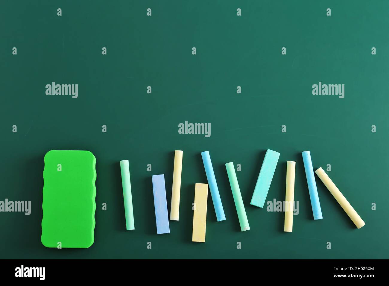 Pieces of chalk and blackboard duster on green background, top view
