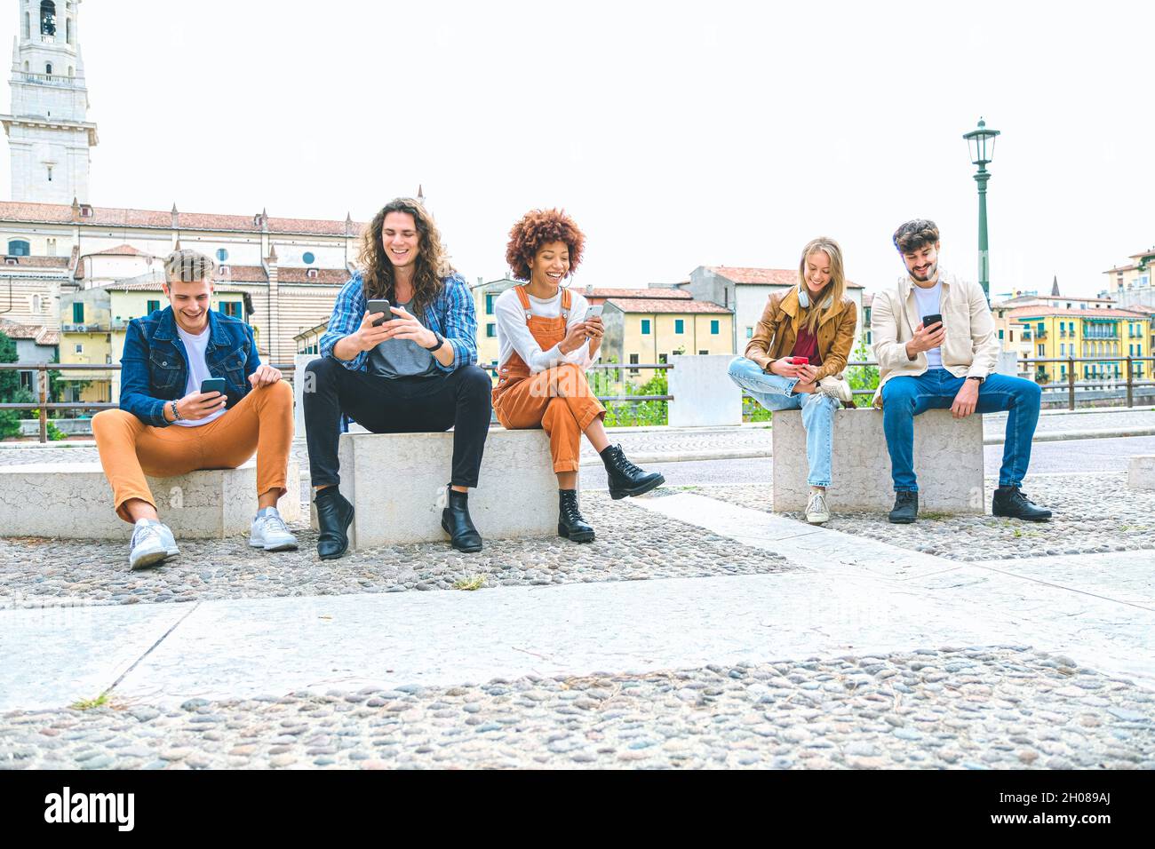 Multicultural group of friends using mobile phones - Students sitting in a row and typing on smartphones Stock Photo