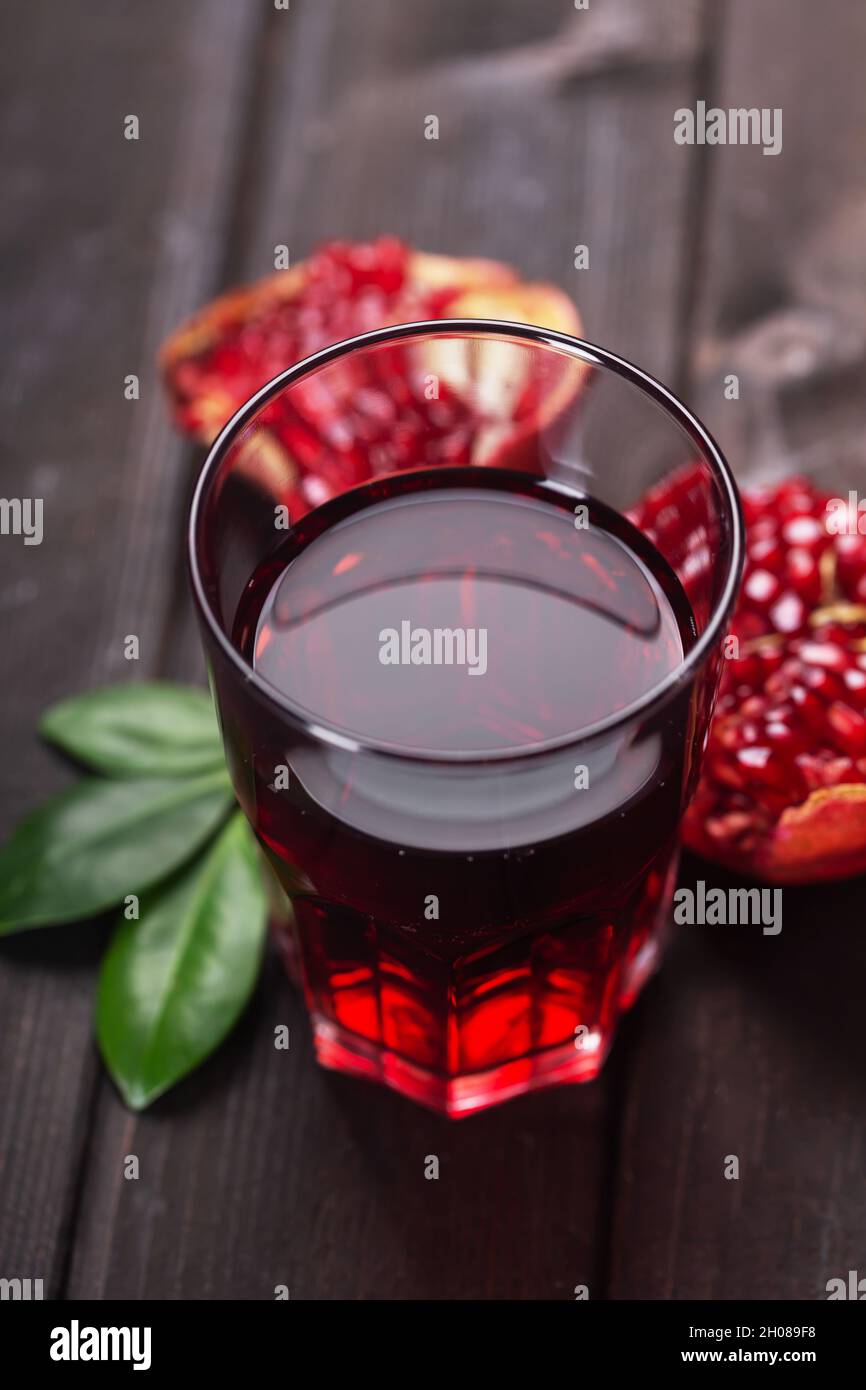 Glass of pomegranate juice with pieces ans leaves of pomegranate fruits