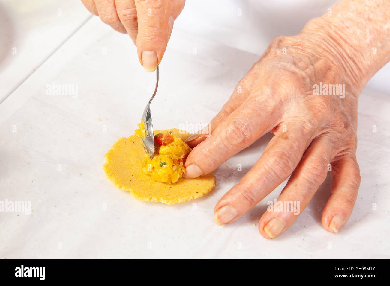 Preparation of the traditional patties from the region of Cauca in Colombia, called empanadas de pipián - Senior woman filling the patties Stock Photo