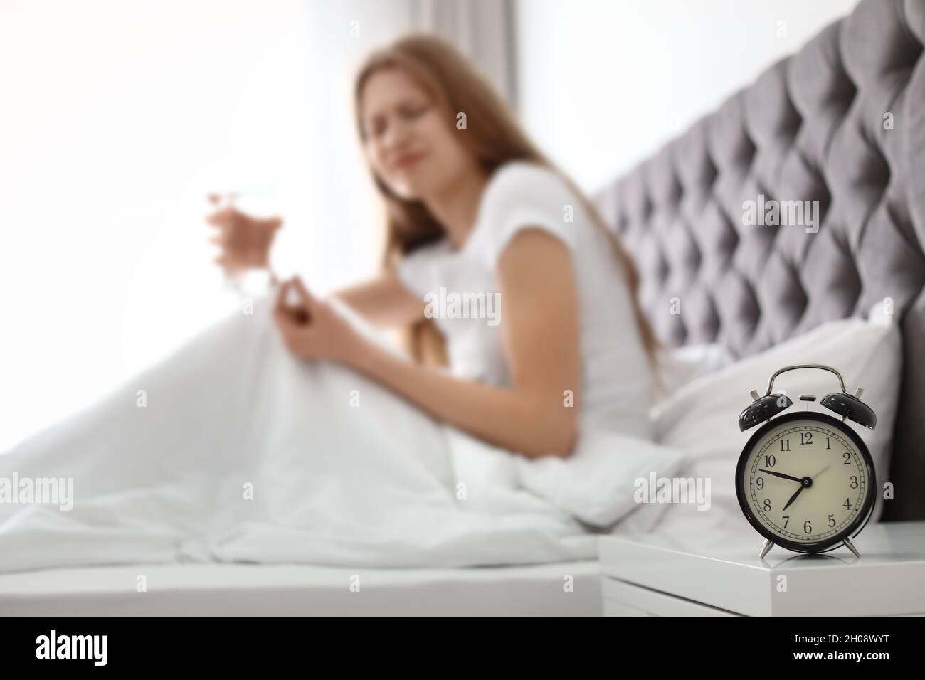 Alarm clock on nightstand of young woman suffering from headache Stock