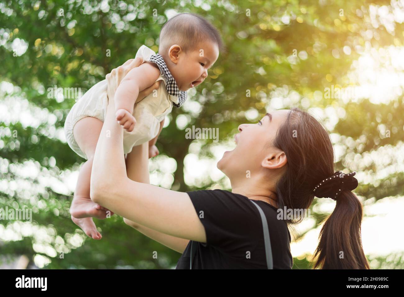 mother holding baby newborn in her arms lifting up on a green nature