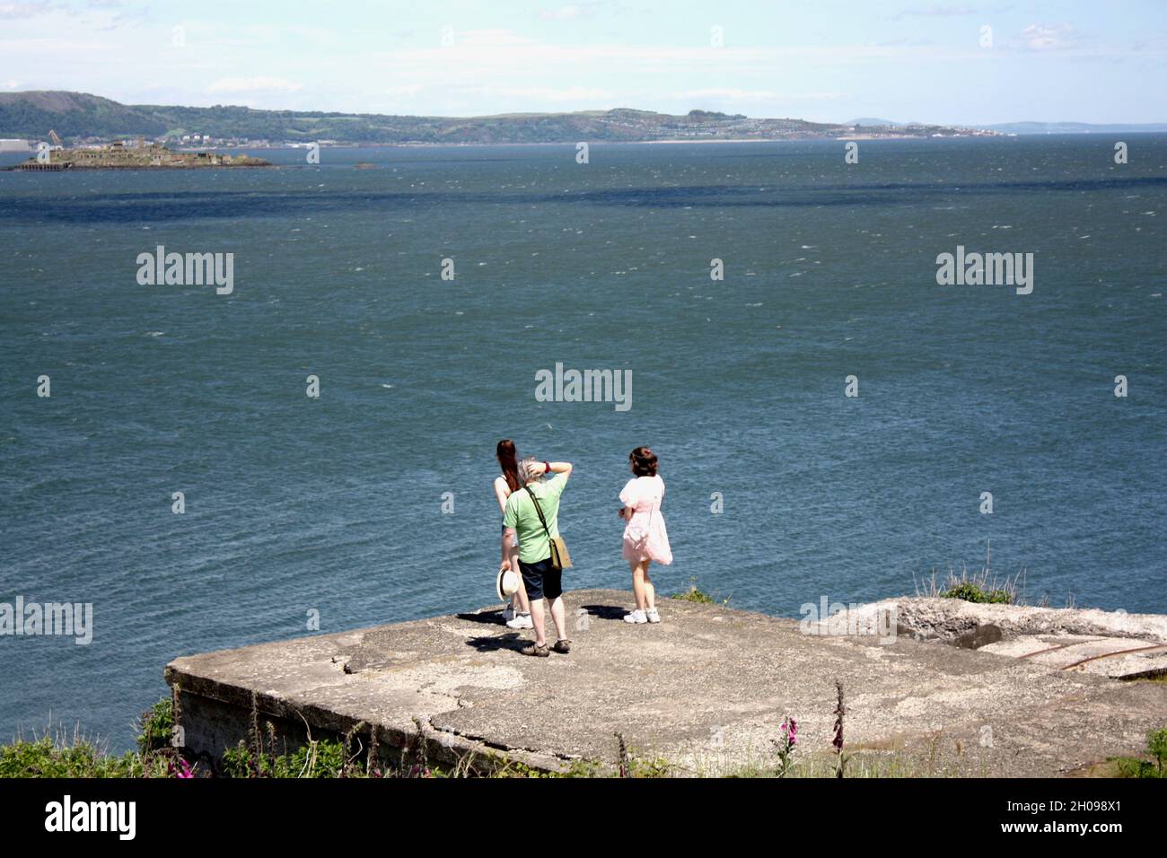 A family stand looking out at the fake warship, Inchmickery Island, by Cramond Island, near Edinburgh. Stock Photo