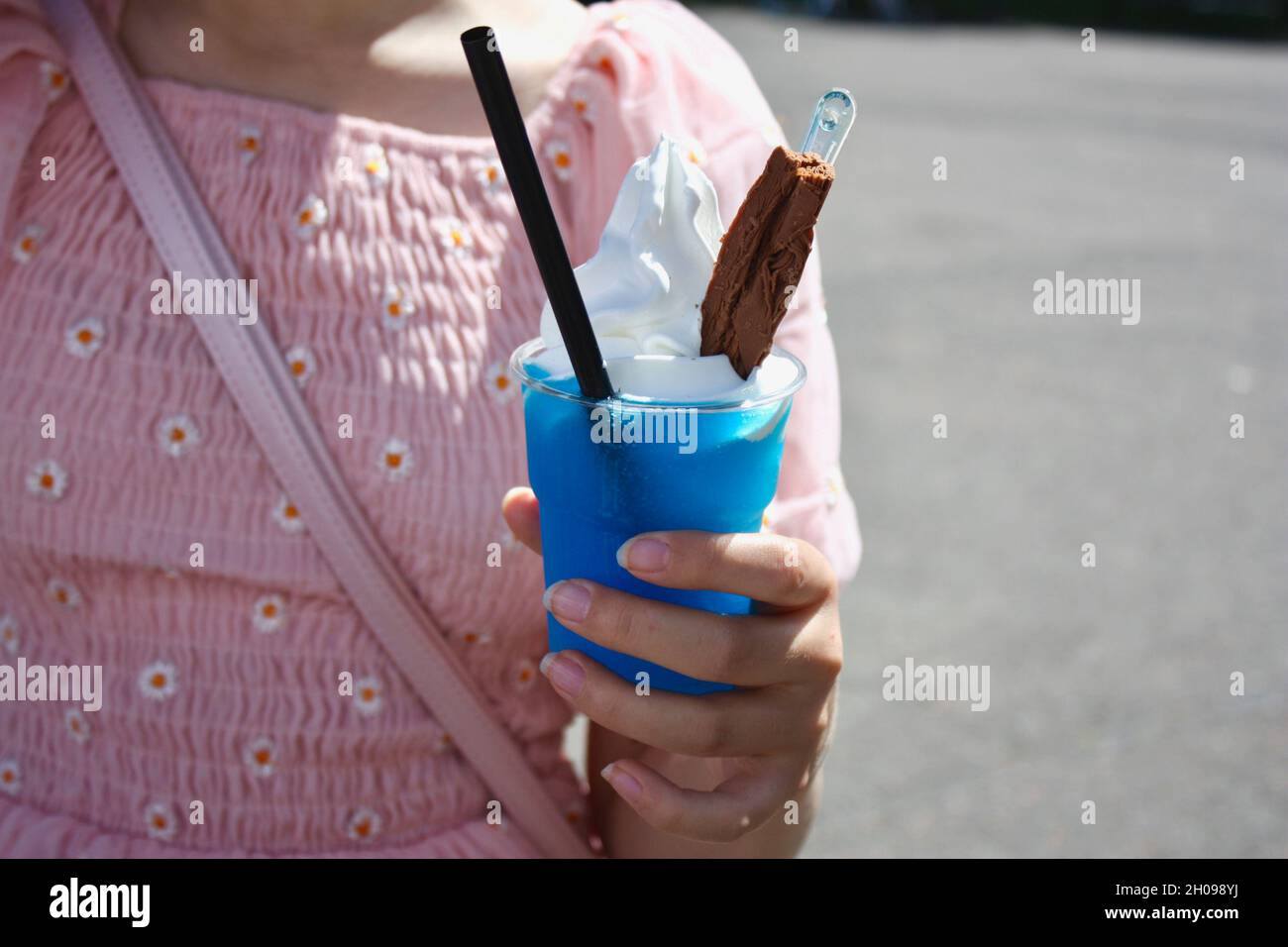 Young teen girl in a pink floral dress holds a blue slush with soft serve ice cream atop. Stock Photo