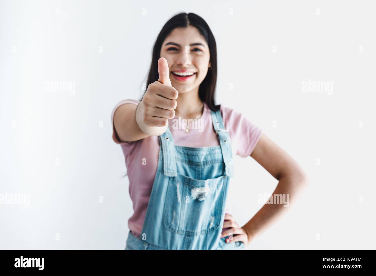 young latin woman smiling and showing thumbs up on a white background in Latin America Stock Photo