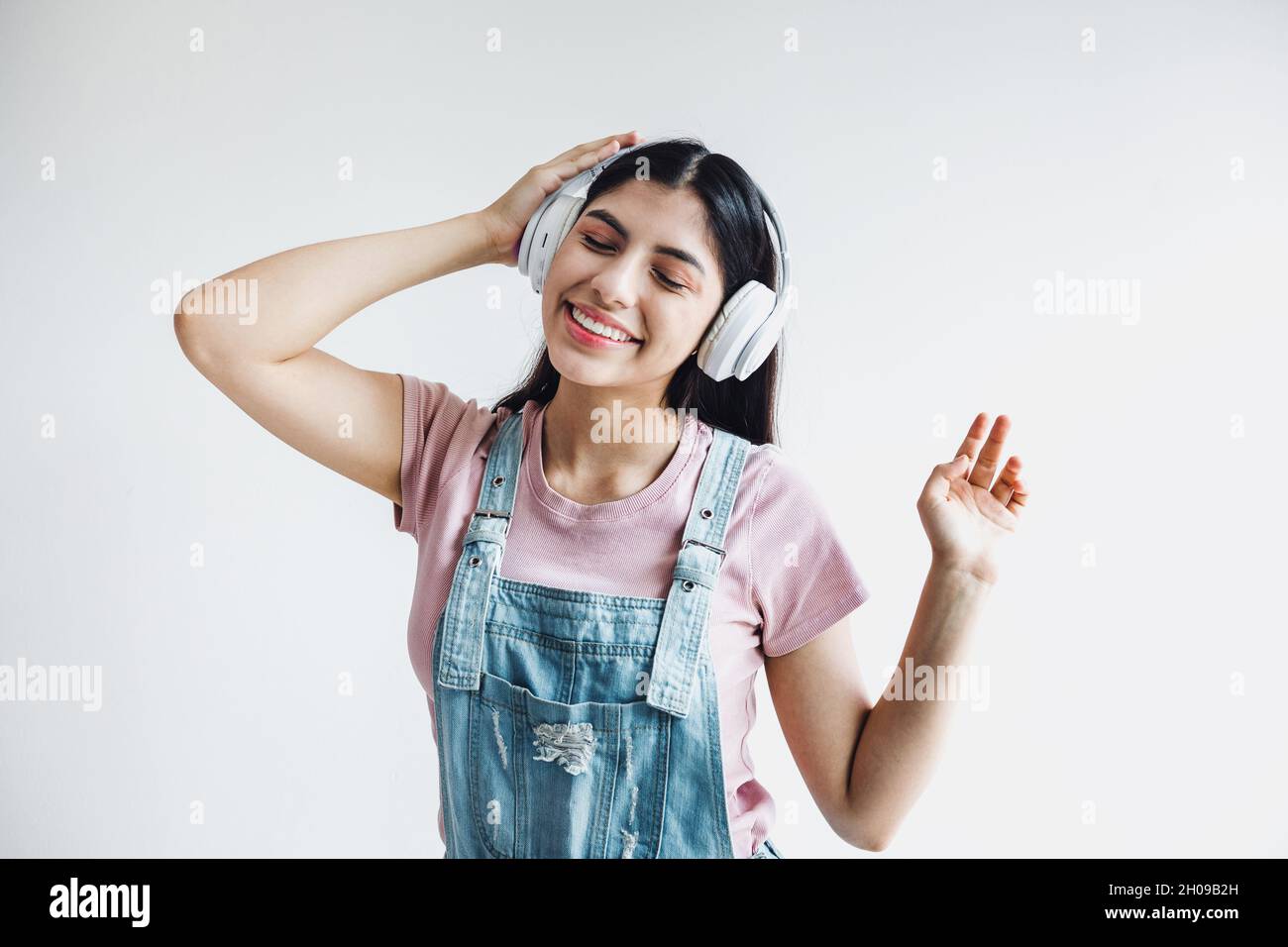 portrait of latin young smiling woman with headphones, dancing and listening music on a white background in Latin america Stock Photo