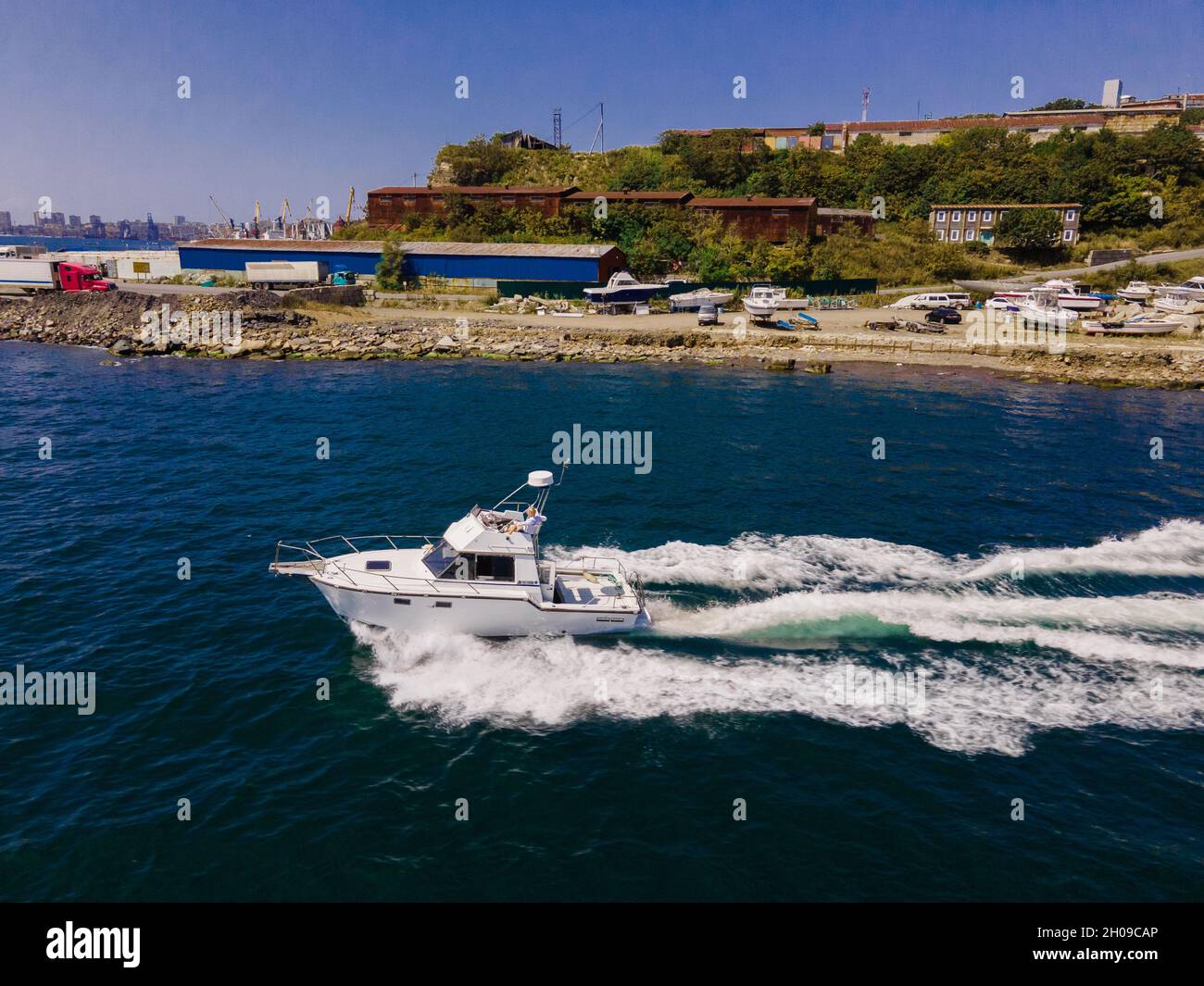 A white boat goes at full throttle along the shore. Photo from the drone, from the side. Stock Photo