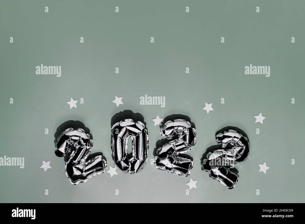 New Year 2022 or Christmas green background flat lay. Top view on 2022 balloon silver or metallic numbers with white star shapes. Invitation or greeti Stock Photo