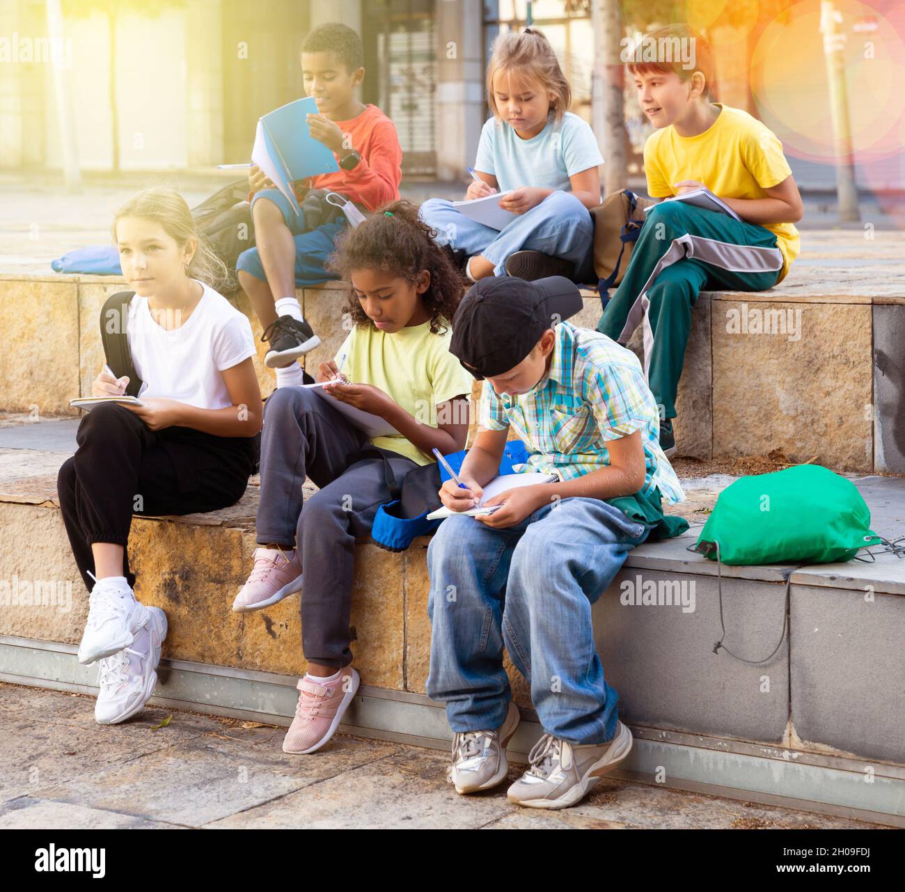 Tweenagers studying outside school, writing in workbooks Stock Photo
