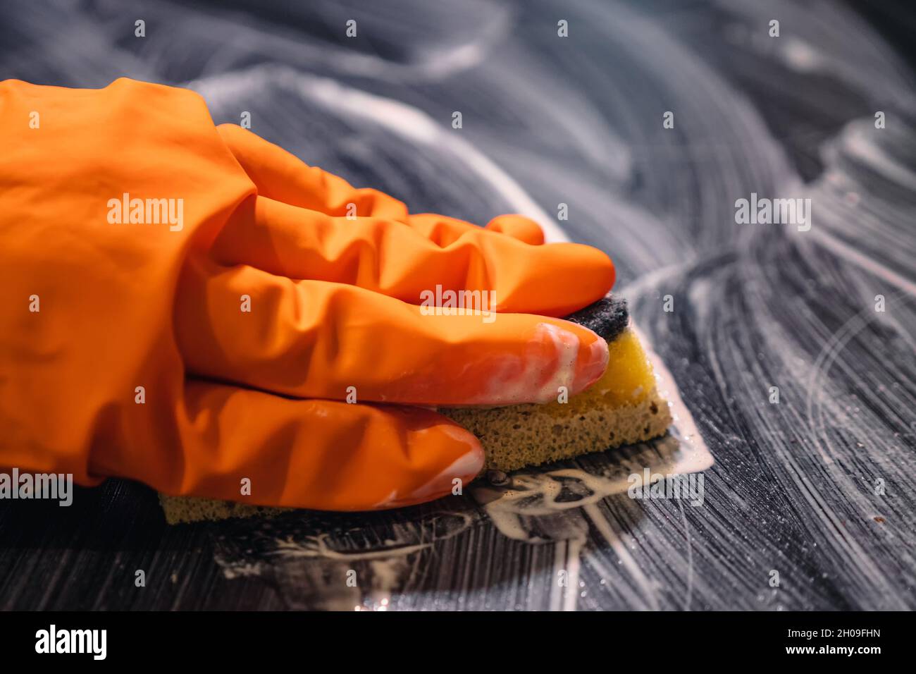 Closeup of orange glove sponge and cleaner washing the cooktop