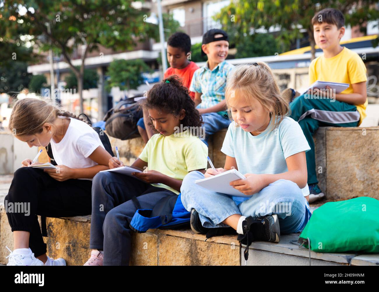 Tweenagers studying outside school, writing in workbooks Stock Photo