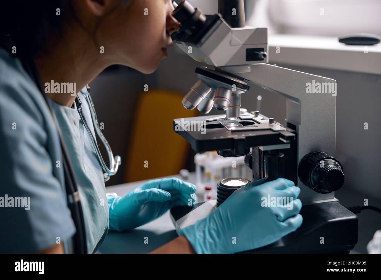 Skilled lab employee in latex gloves reaserches sample looking into microscope in laboratory