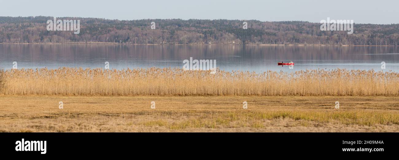 Seeseiten, Germany - Feb 23, 2021: Scenic landscape at Starnberger See with red canoe and reed. Panorama format. Stock Photo