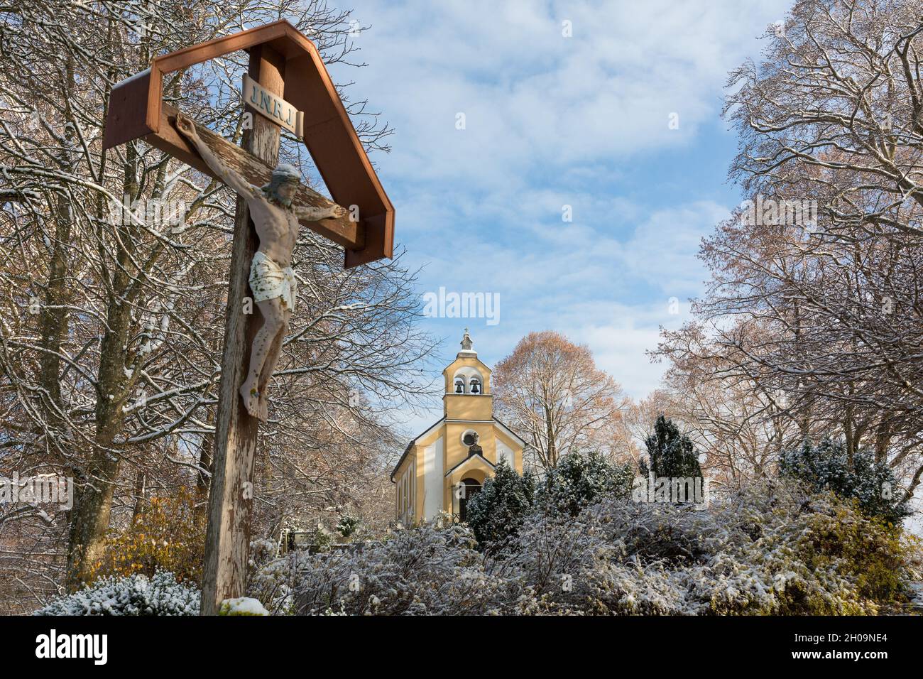 Winter landscape with Jesus on the cross and a small chapel. At the cemetery of Andechs. Stock Photo
