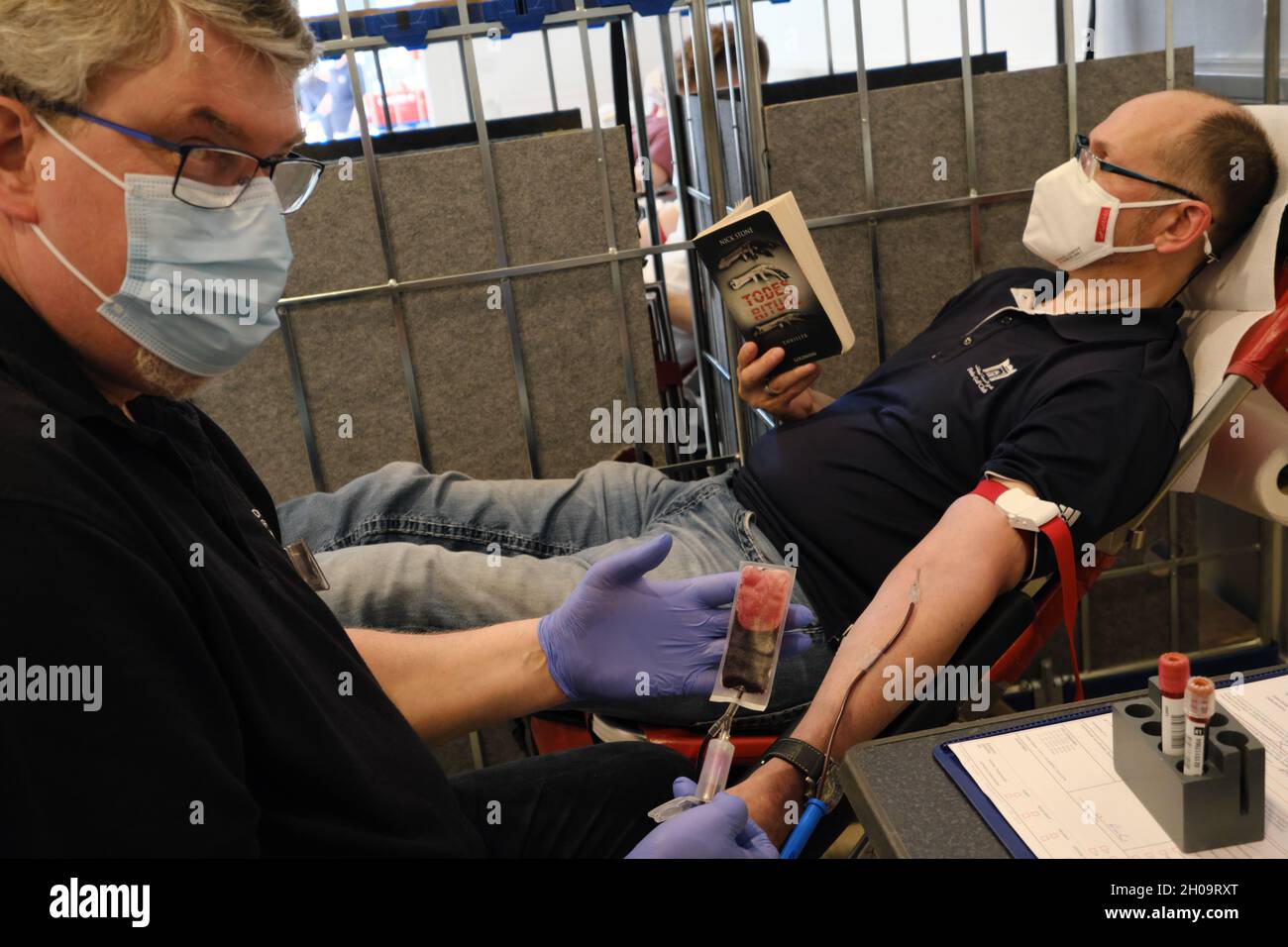 '14.06.2021, Germany, Bremen, Bremen - Blood donation for the German Red Cross, employee lays the canula, donor reads crime novel. 00A210614D123CAROEX Stock Photo