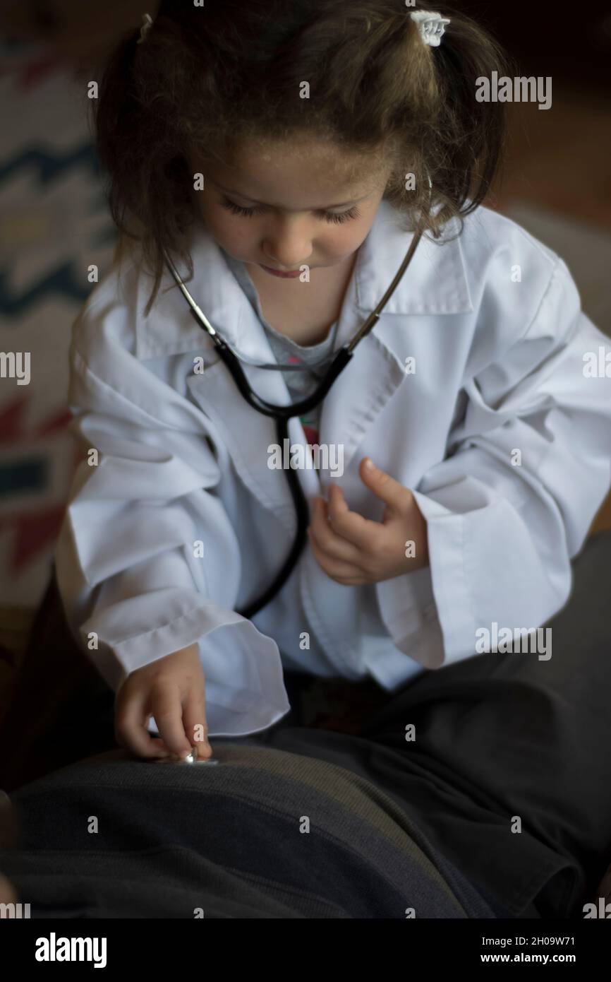 A little girl in a doctor's coat examines her grandfather with a stethoscope. children's games Stock Photo