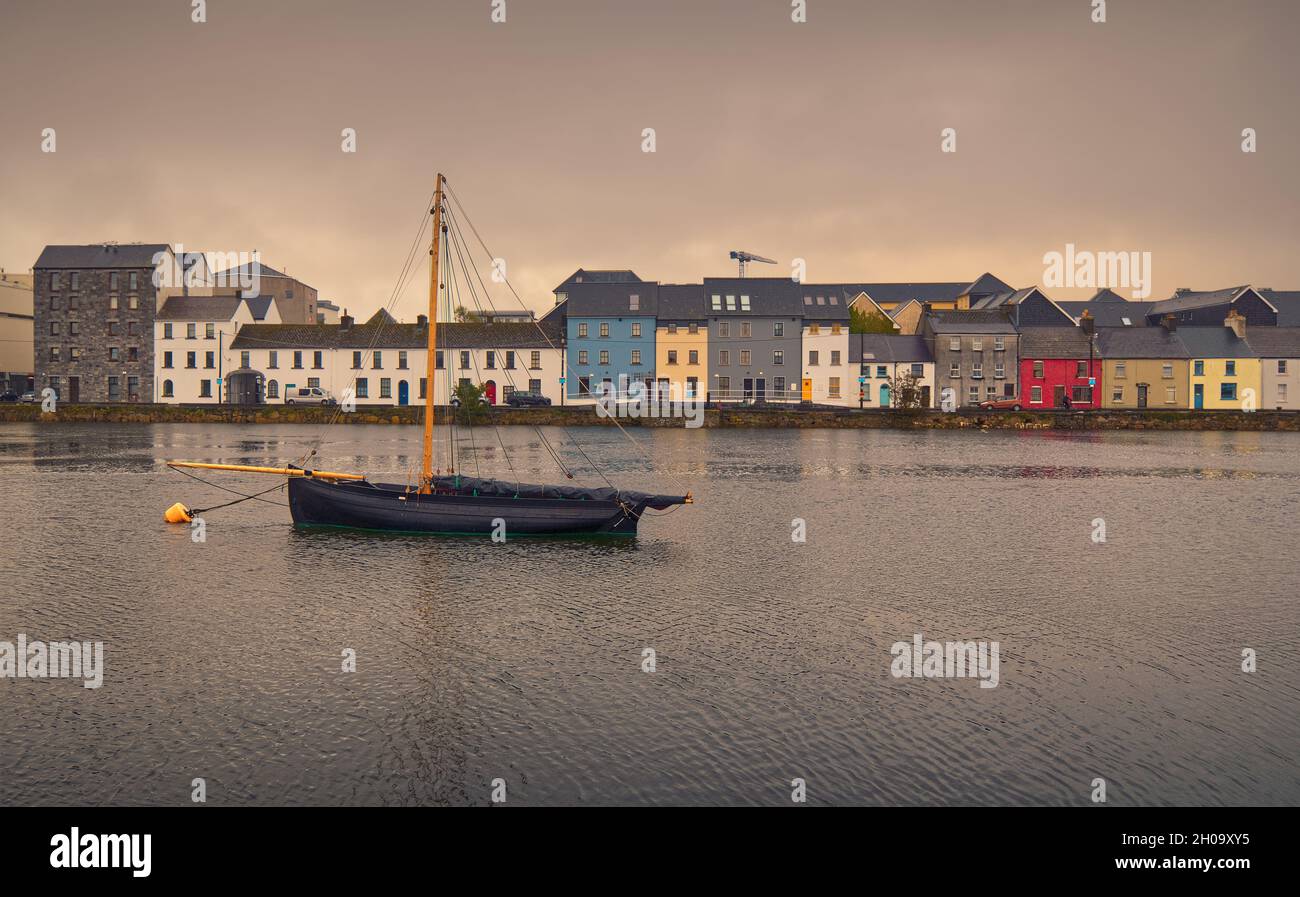 Beautiful cityscape scenery with old wooden fishing boat named Galway hooker in the Corrib River with colorful houses in the background at Claddagh in Galway city, Ireland Stock Photo