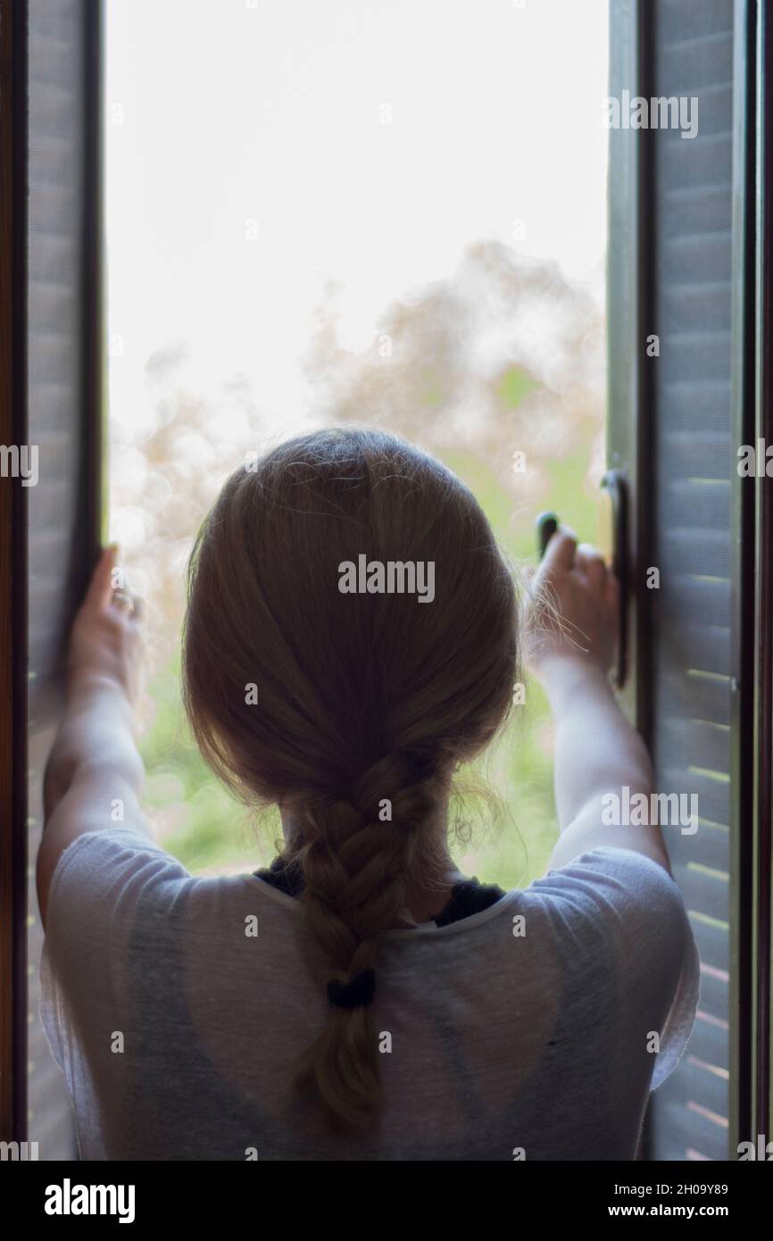 The young woman watches the garden of her house through the barred