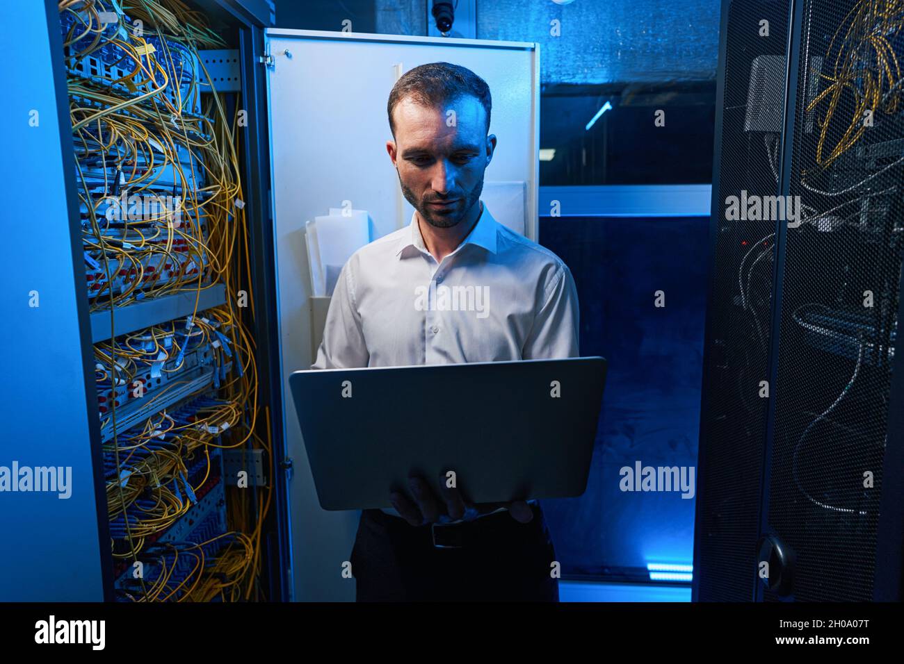 Man using laptop near open server cabinet Stock Photo