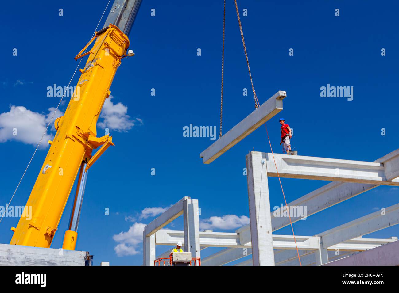 Worker is helping mobile crane to manage concrete joist for assembly ...