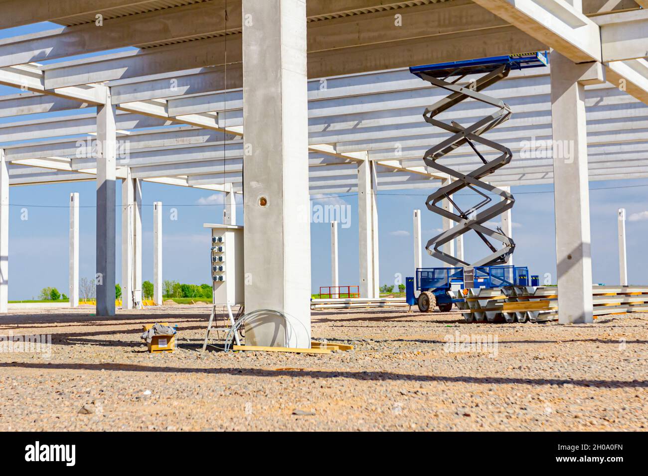 Scissor lift platform with stretched hydraulic system at maximum height range under building skeleton. Stock Photo
