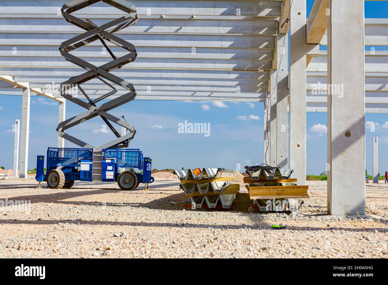 Scissor lift platform with stretched hydraulic system at maximum height range under building skeleton. Stock Photo