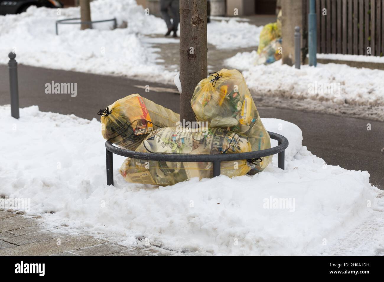 Starnberg, Germany - Jan 19, 2021: Several yellow garbage bags (Gelber Sack) with recyclable waste. At a sidewalk, during winter. Stock Photo