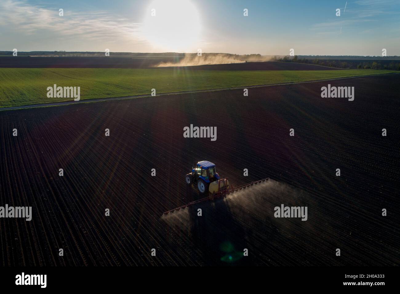 Tractor spraying artificial fertilizer on soil in spring time. Shoot from drone at the evening Stock Photo