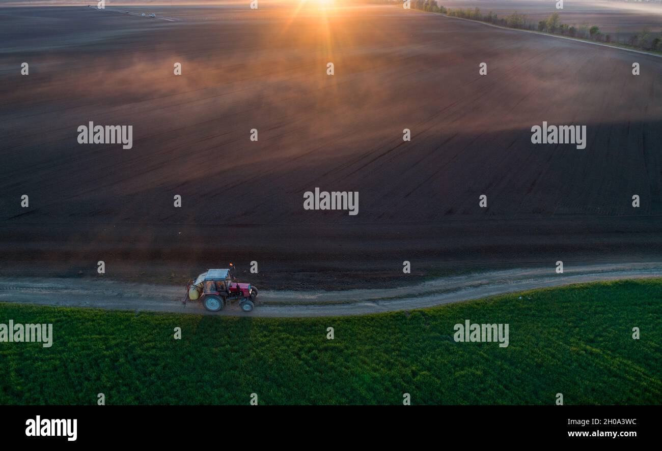 Aerial image of tractor driving on dirt road with equipment for soil spraying, shoot from drone Stock Photo